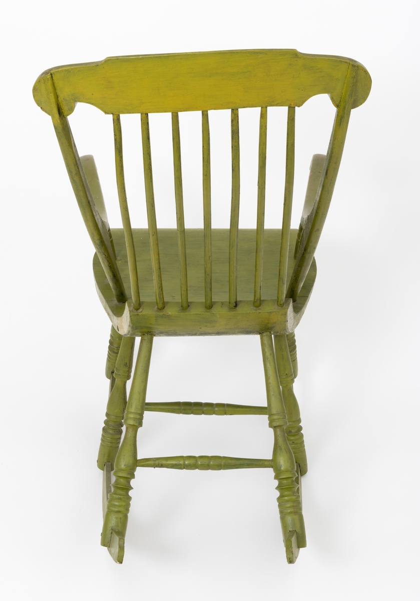 Stol, gyngestol, med seks ben på to meier. Stolen er påført grønn farge, sannsynligvis oppå en opprinnelig svart farge. (Setet er på undersiden svartmalt.) Konstruksjonen kan minne om slik pinnestolene er sammenføyd. Bena er dreid og tappet inn under setet. De to meiene er felt inn i (opp i) utskårne spalter i stolbena. Det er dreide sprosser, mellomstykker, mellom hvert benpar, foran, på midten og bak.  Setet buer nedover i framkant, og oppover i bakkant. Stolen har sju trespiler i ryggen som er tappet i setet og toppstykket. Armlenene er delvis felt inn i ryggstolpene (rygstavene). Armlenene er forsterket med metallbeslag. Det er to dreide sprosser (støtteben) under hvert armlene, disse er tappet inn i armlenet og setet. Toppstykket på stolryggen er felt inn i  og skrudd fast til ryggstolpene (ryggstavene) på stolryggen. Stolryggens ryggstolper er tappet ned i setet.