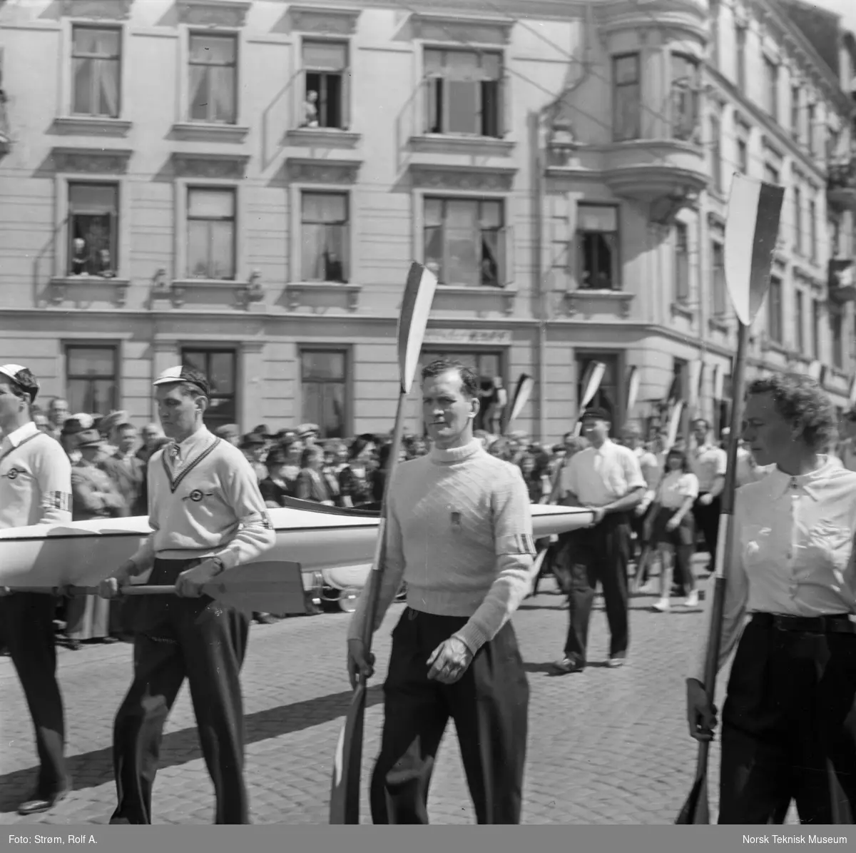 Opptog under Idrettens dag med tre mannlige og en kvinnelig idrettsutøver med padleårer og kano i første rekke, Lille Bislett, Sofies gate, Oslo, juni 1945.