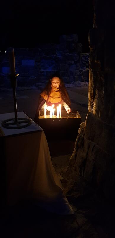 En middelalderkledd ung kvinne tenner levende lys under ruinbuene i Hamardomen. (Foto/Photo)