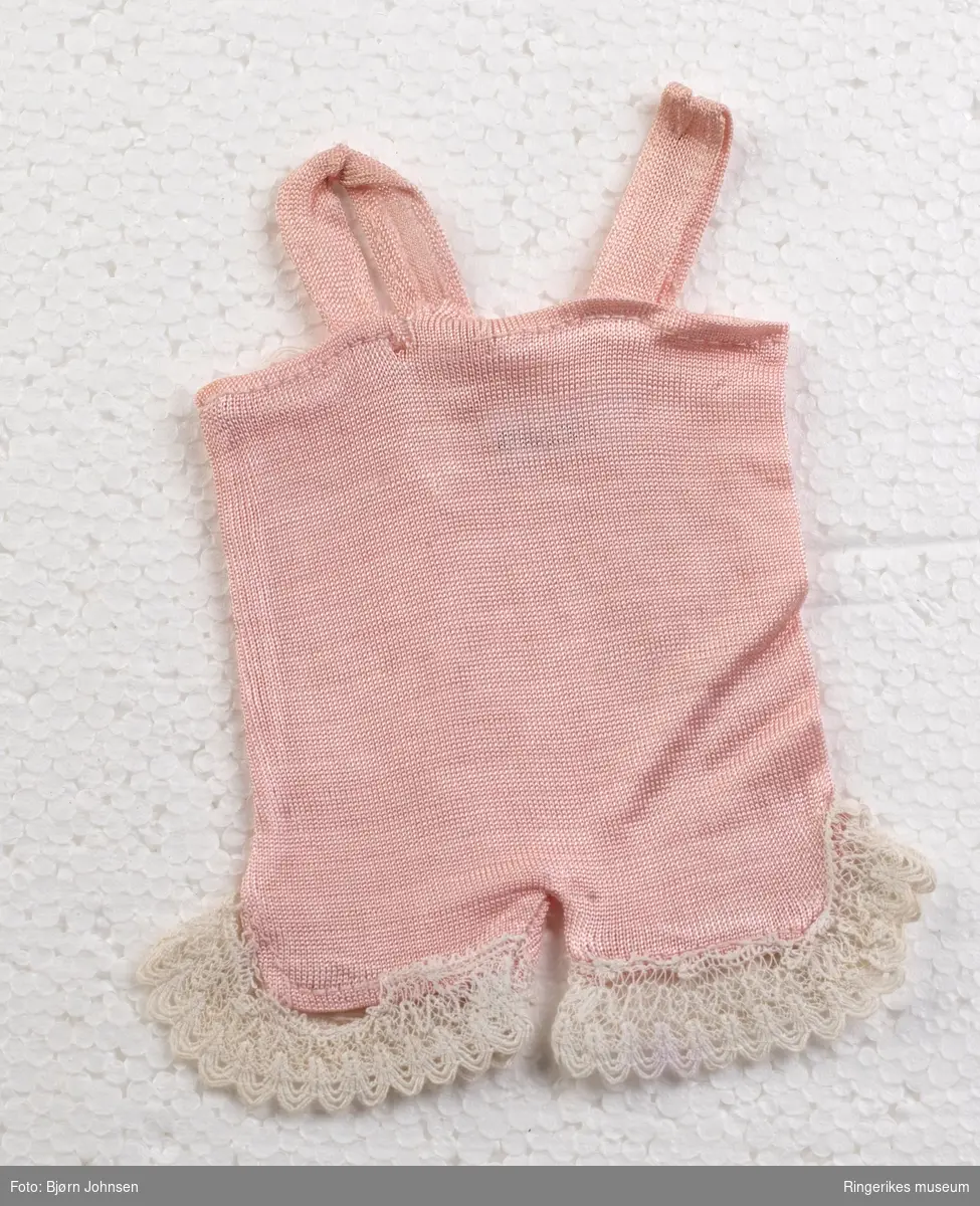 Hjemmesydd rosa seleshorts i polyester. Påsydd hvite blondebånd på beinkantene. Reparert med håndsøm og hvit tråd på baksiden.