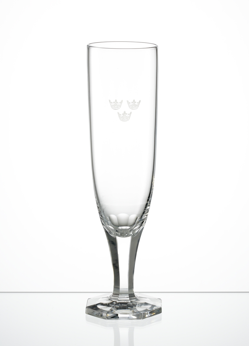 Design: Edward Hald, Orrefors. 
Champagneglas med tre kronor graverade på kupan. Facettslipat ben och åttkantig fot.