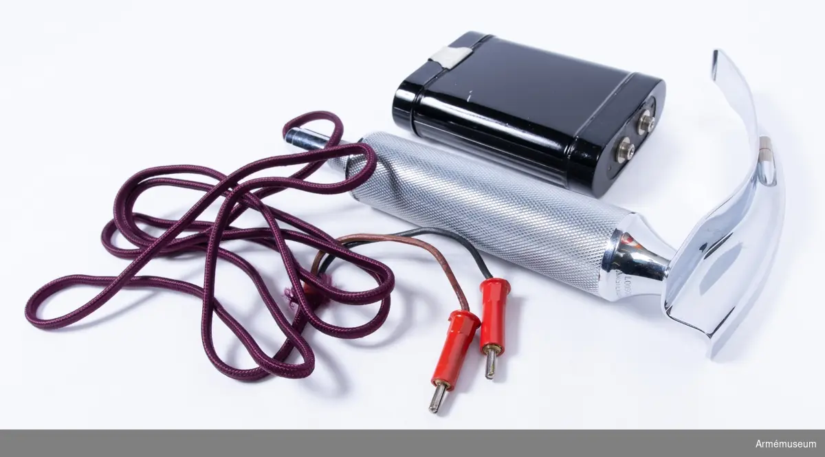 Cylinderformat metallhandtag med lila elsladd och medföljande svart batterihållare med batteri i. På handtagets topp finns ett nedåtböjt metallblad med en kant på höger sida av bladet där en lampa är monterad. Handtaget är märkt "Loosco, Amsterdam". Laryngoskop används vid undersökningar av stämbanden eller som hjälpmedel för att föra in en slang i luftstrupen för ventliation, dvs. när en respirator/ventilator ska kopplas in.