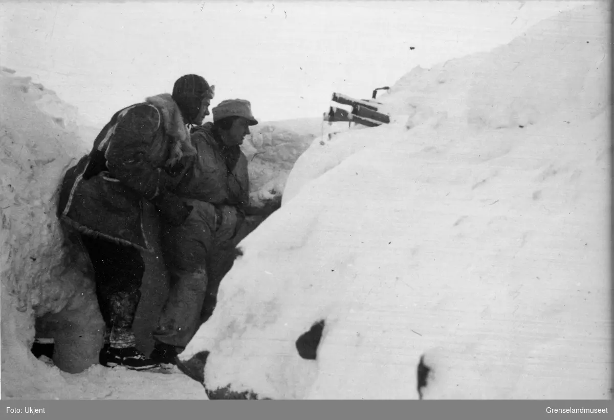 I fremre stilling. To soldater står i dekning i en skyttergrav bygd opp av snø. I snøveggen er det plassert flere skafthåndgranater med kapselen til utløsersnora skrudd av. 