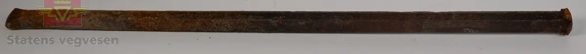 Sekskantet bor i metall, med slagflate i den ene enden og meiselformet skjær i den andre enden. Boret ser ut til å være godt brukt.
