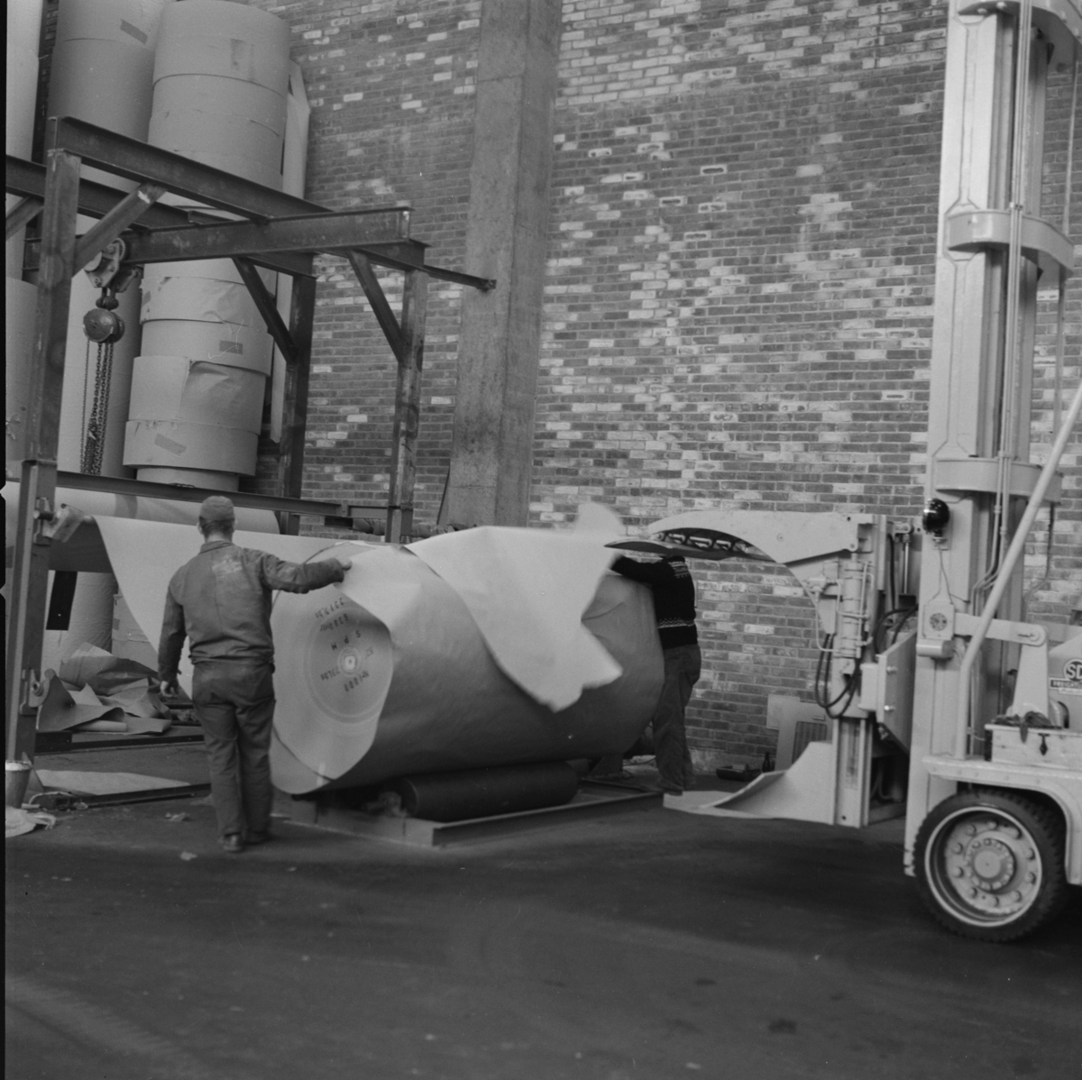 Fra papirfabrikken Sande Papermill. En mann overvåker prosessen. med Stor rull med papir og Truck med gripeklo. Ca. 1960-63