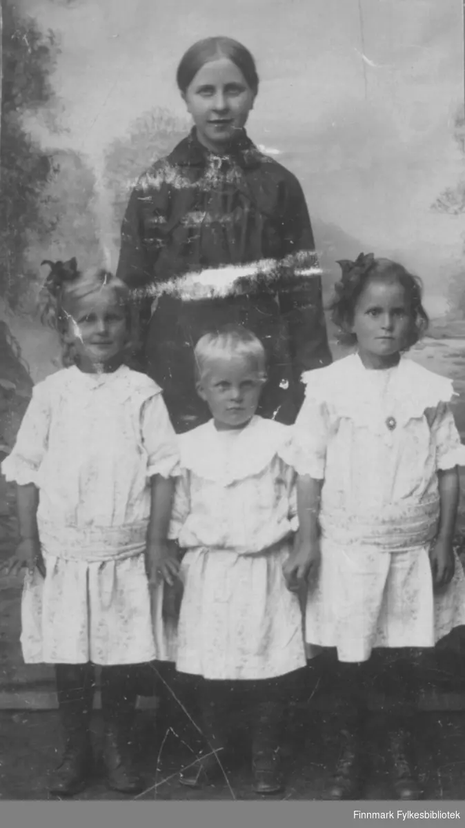 Mor kledd i svart kjole med tre jenter kledd i hvite kjoler.