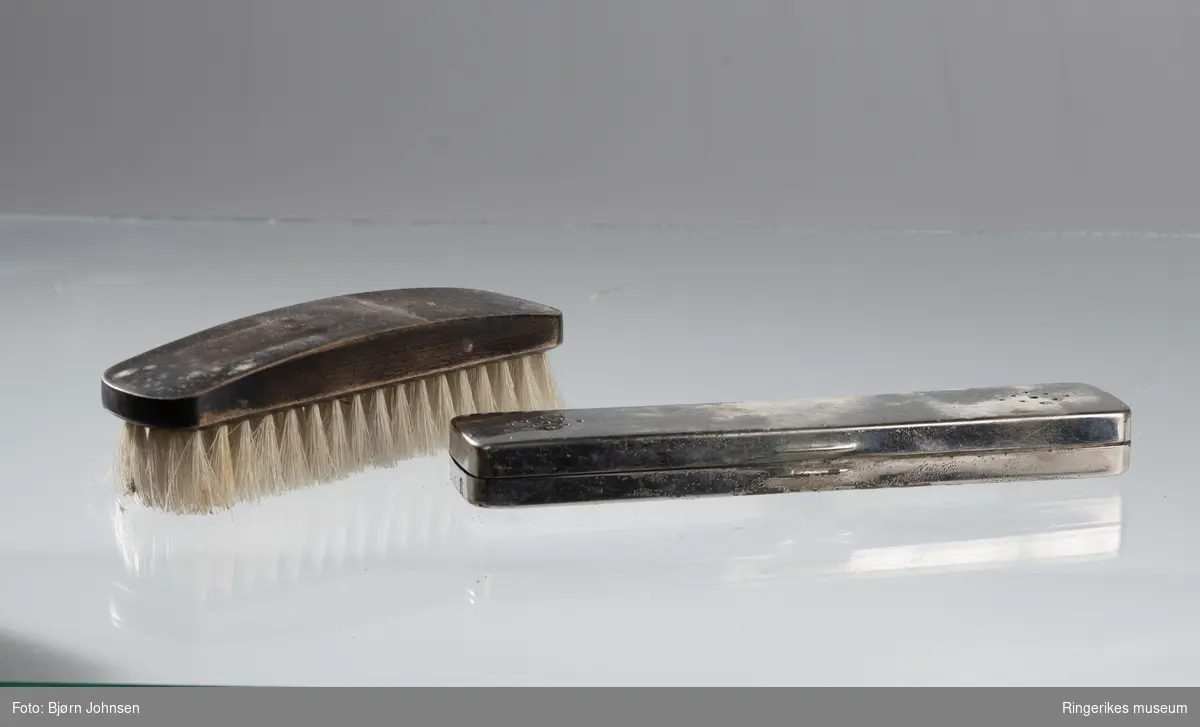 Svart tannbørste i hard plastikk med hvit bust. Tannbørsten ligger i et ståletui med hengsler og luftehull på undersiden.