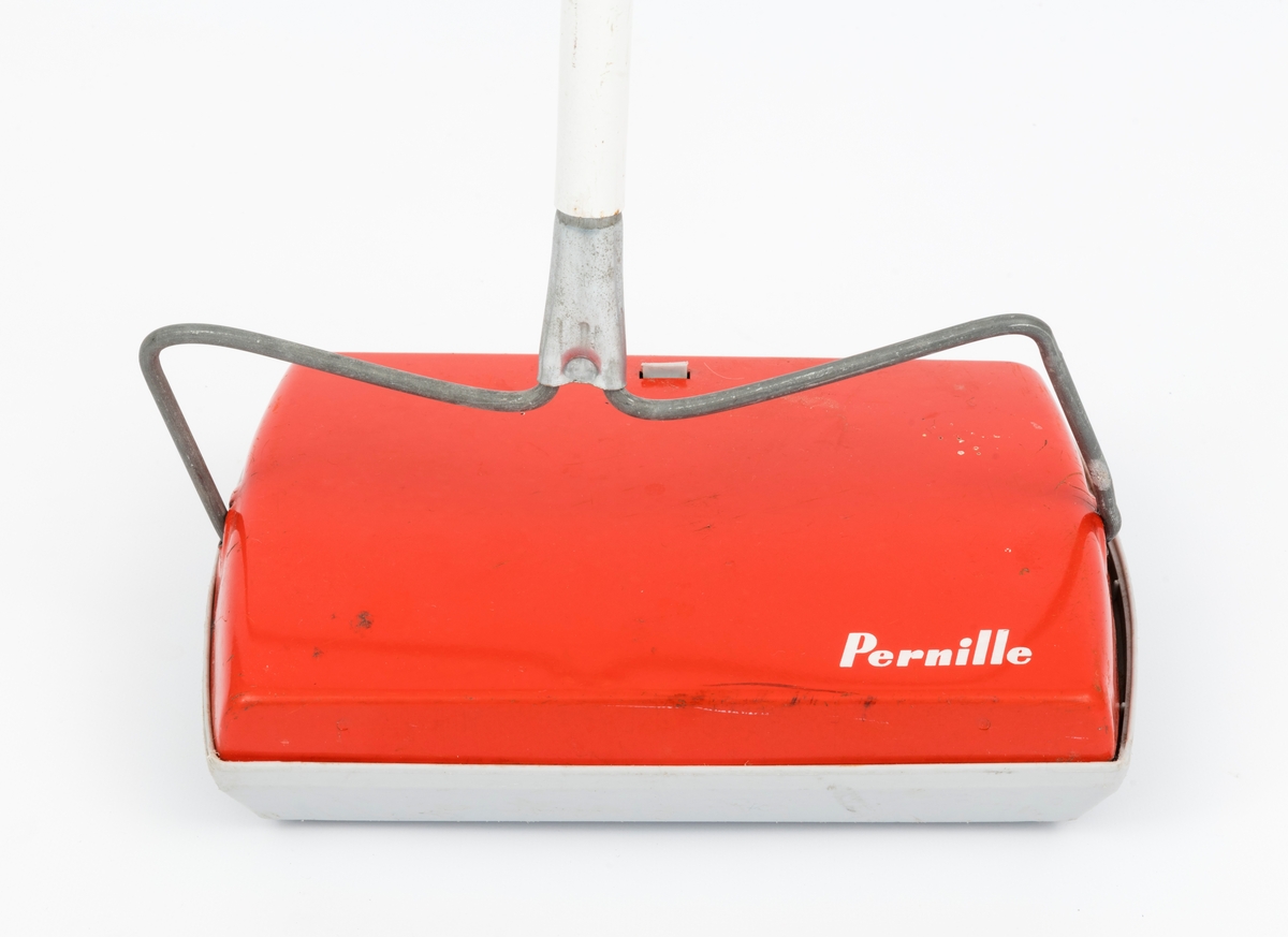 Apparat til manuell børsting av tepper. Hvitt skaft (i tre deler) og selve apparatet i oransje-rød farge på oversiden med påskrift "Pernille". På undersiden er fire hul i plast og en børste som roterer.