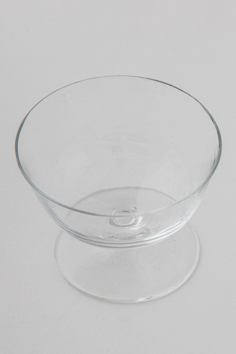 Likørglass i meget tynt klart glass. Konisk kupa med svakt utoverbrettet munningsrand, som bæres av en meget tynn stett. Sirkulær fotplate, noe hevet på midten.