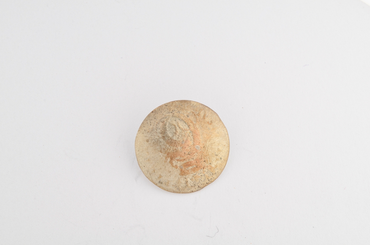 Knapp i sølv, dansk mynt. Rund og lett bua på oversida, utydeleg dekor av ei krone. På undersida IIII SKILLING DANSKE 1695. Hempe i messing pålodda på undersida.