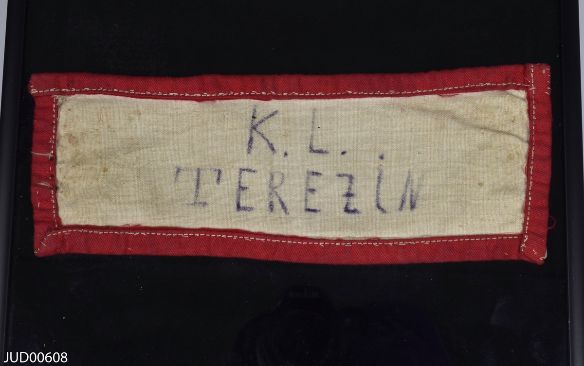 Två monterade armbindlar märkta med K.L. Terezin. Den ena armbindeln har en röd kant och den andra har en rosa kant.