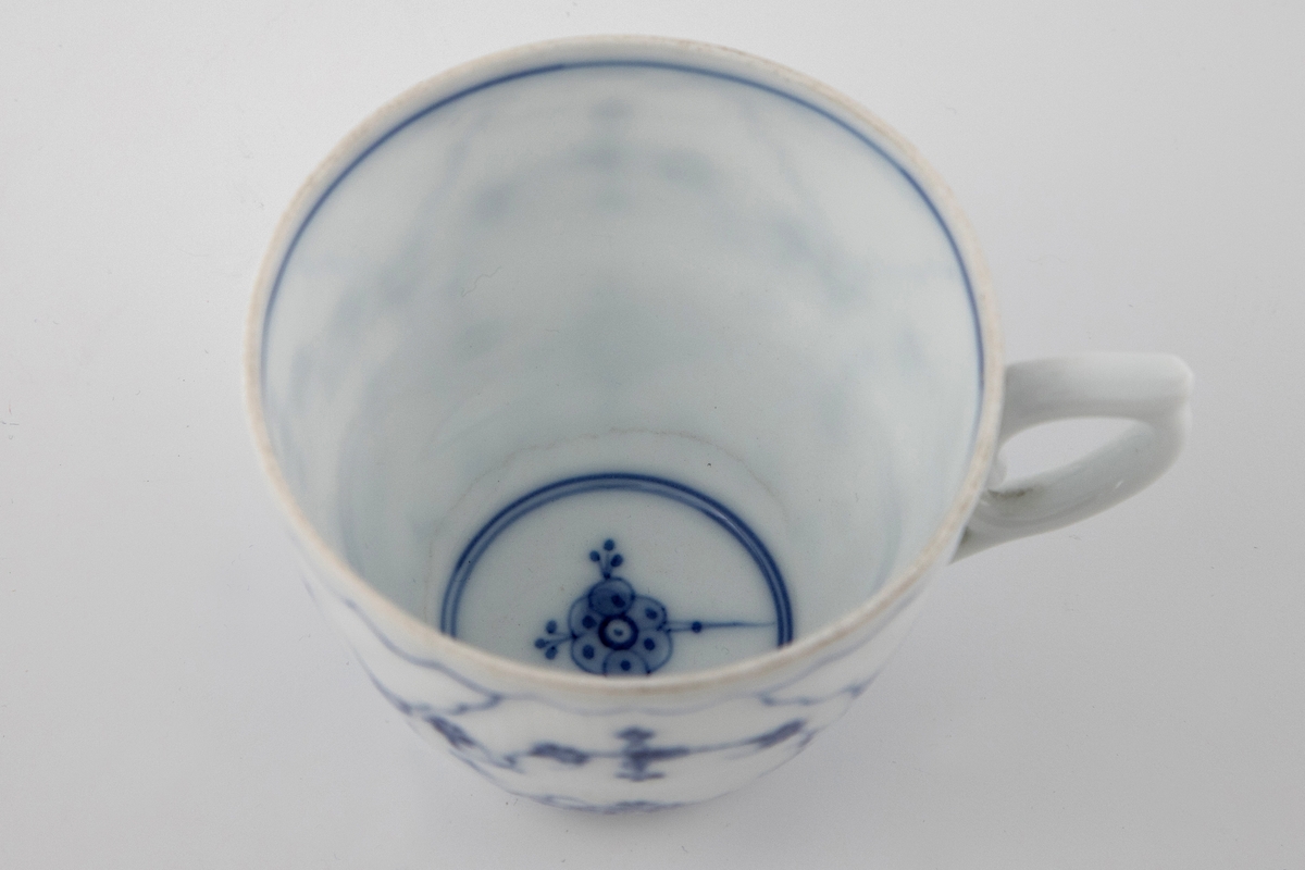 Kopp med skål i glasert porselen, dekorert med koboltblå underglasurmaling i form av stråmønster. Vertikale riller på koppen, mens skålen har radiære riller.