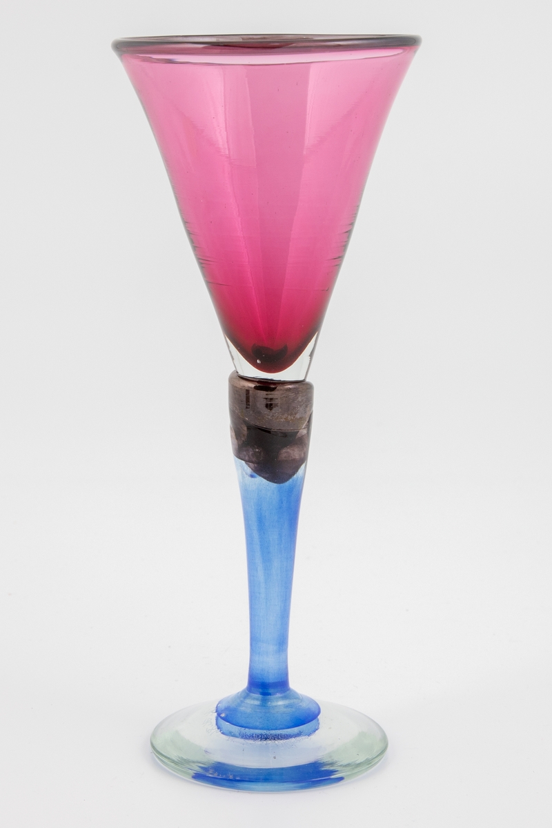 Vinglass med lillafarget konisk kupa, som hviler på en stett i blålig glass. Munningen er markert med mørkt glass. Foten er svakt buet og i klart glass.