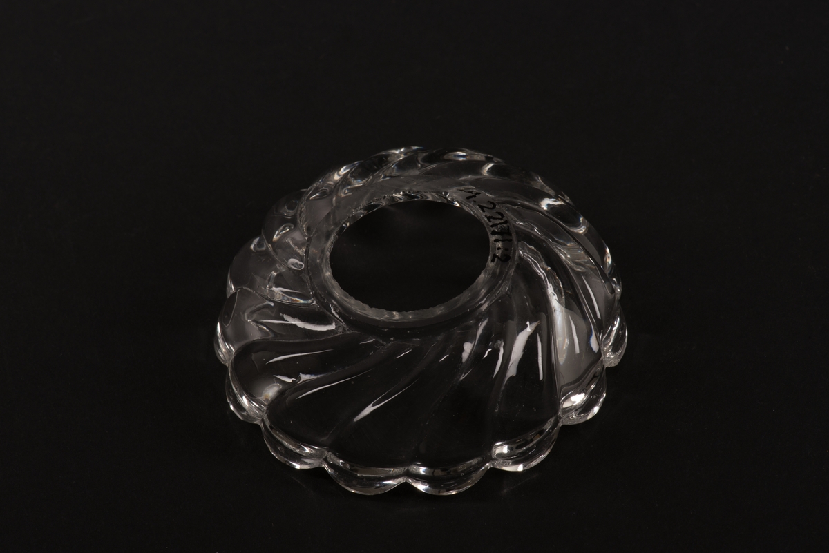 Rund ljusmanchett av ofärgat pressglas. 
Pressad yttäckande konvex och konkav dekor av spiralvridna åsar som avslutas i en vågformad kant. 
Ingår i Reijmyre glasbruks serie Turbin.