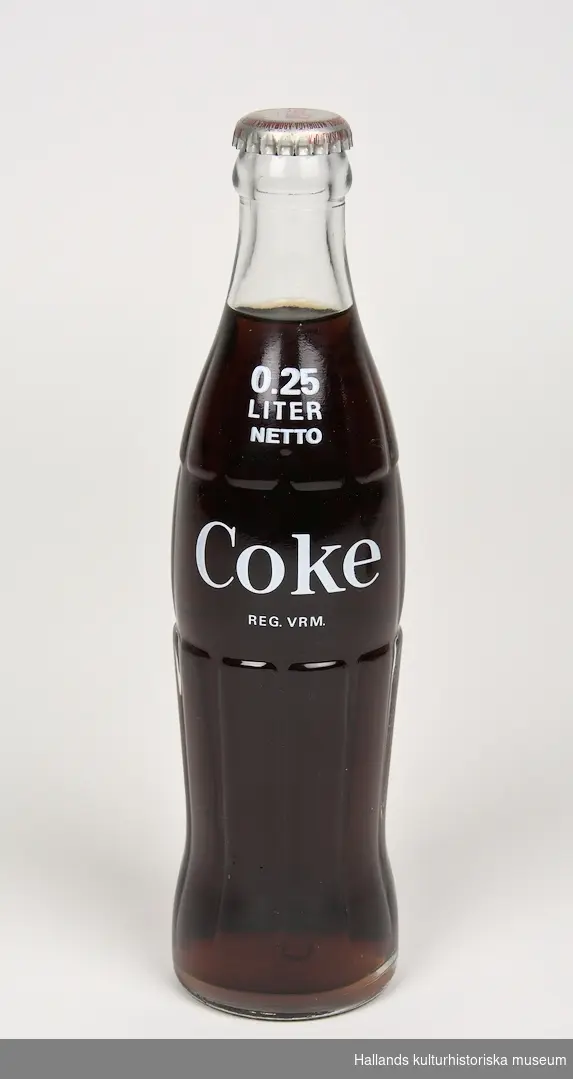 Läskedrycksflaska: Coca-Cola. Flaskan är tillverkad av klart glas. På flaskans bröst finns ett vitt tryck i form av en "Coca-Cola"-logotyp samt text. 250ml. Oöppnad.