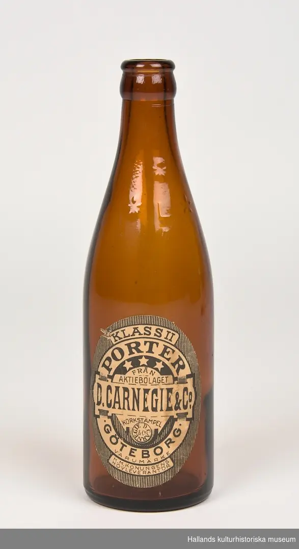 Ölflaska: "D. Carnegie & Co Porter". Flaskan är tillverkad av klart brunfärgat glas och har en tryckt etikett med logotyp samt text. På flaskan finns ett inpräglat "L" (Lyckholms bryggerier) omgärdat av stjärnor.