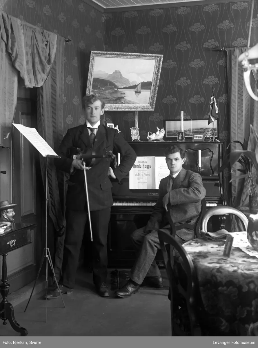 Portrett av to menn med piano og fiolin i stueinteriør