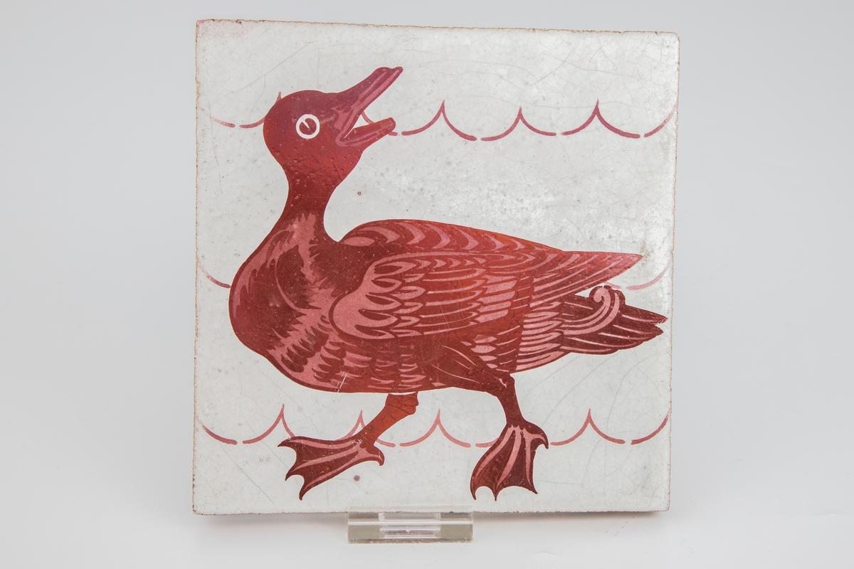 Flis med dyremotiv i rød lusterglasur som avbilder en and.