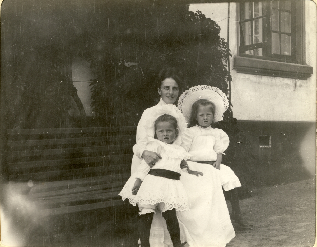 Nini Egeberg med døtrene Lucy og Mimi på en hagebenk på Bogstad gård. Fotografert sommeren 1910.