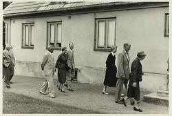 Tre kvinner og fire menn spaserer forbi et bolighus, antagel