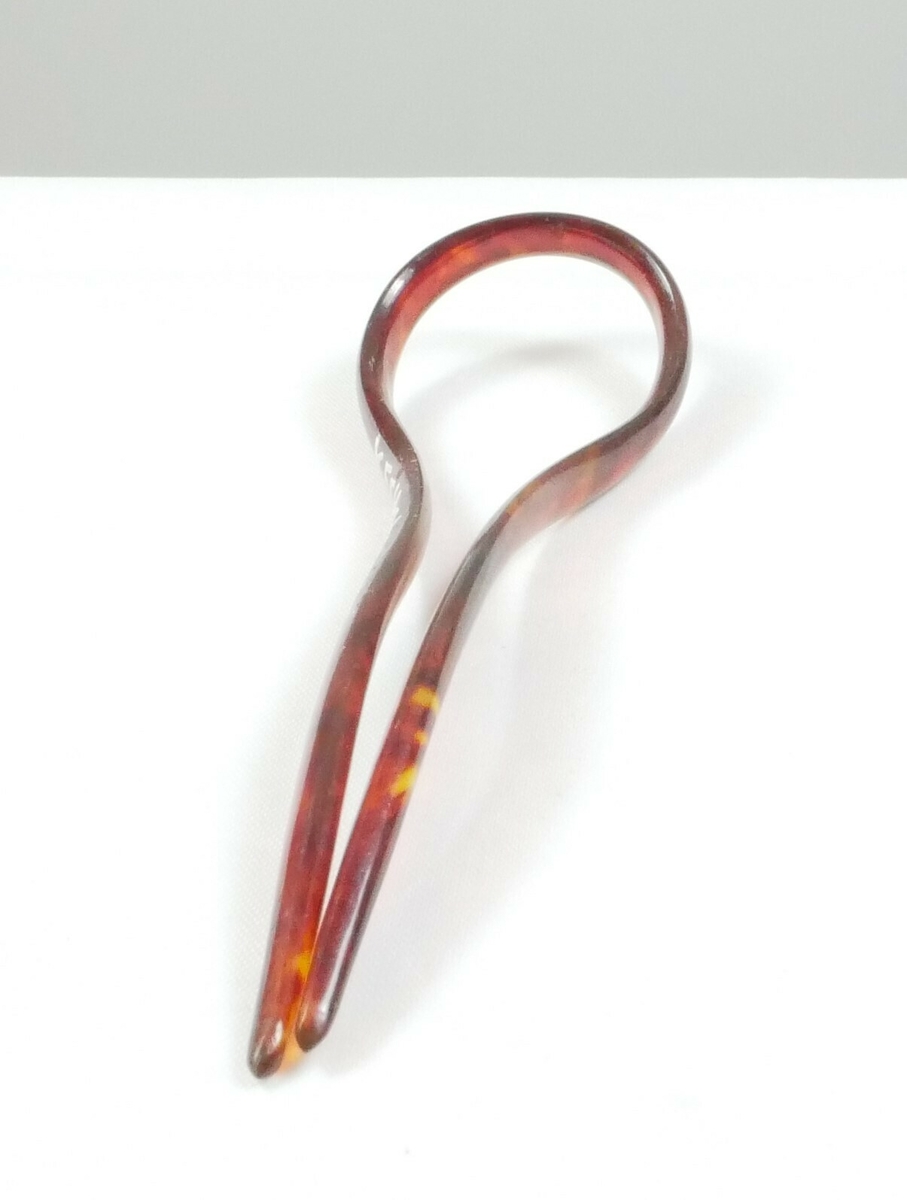Buet brun hårspenne i plast med to lengder til å feste med. Spennen går utover på enden og har en rund form. 