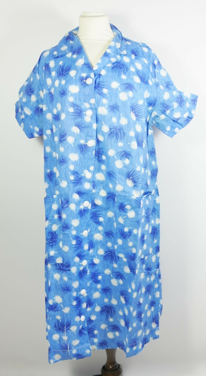 Langermet blått kjoleforkle med mønster i kvitt og mørk blått. To lommer framme og knapper heilt ned.