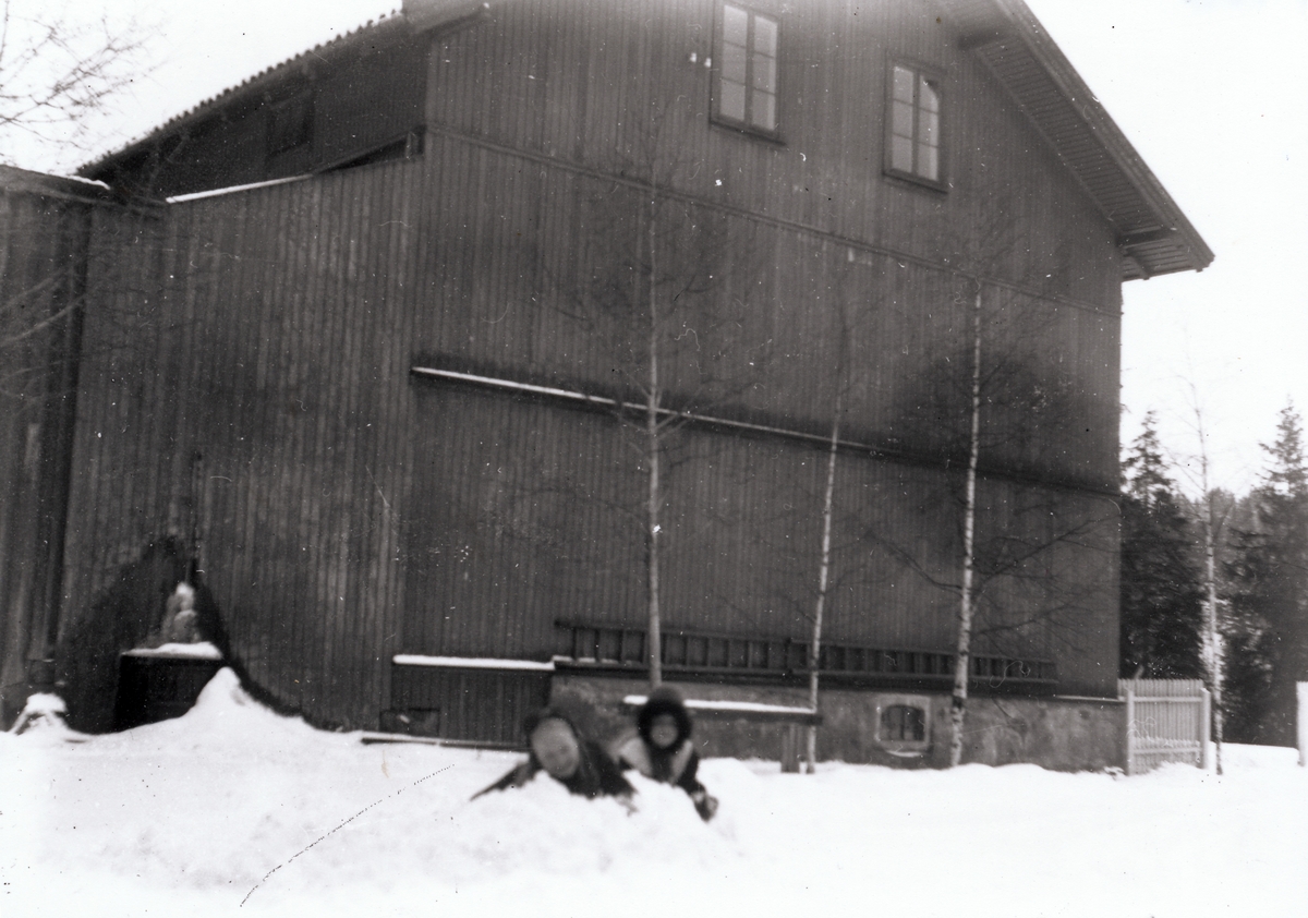 To av bestyrer Rydgrens døtre leker i snøen i hagen utenfor bestyrervillaen på Kistefos. Småjentene leker rett ved kortveggen til den store arbeiderboligen, som sto helt inntil tomta til bestyrervillaen.