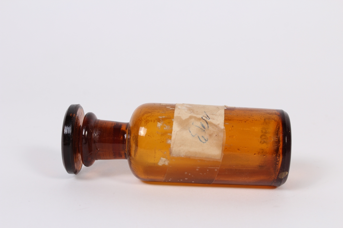 Liten brun glassflaske med kork og etikett. 
Gjenstanden har vore brukt i samband med dyrlegearbeid på Jæren.