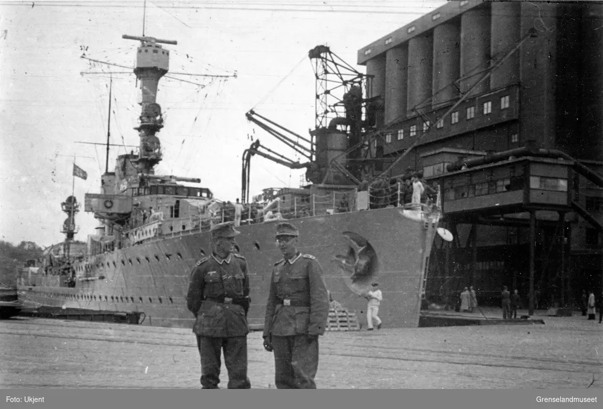 To soldater står på en kai foran et krigsskip. Kan se ut som de er i Oslo.