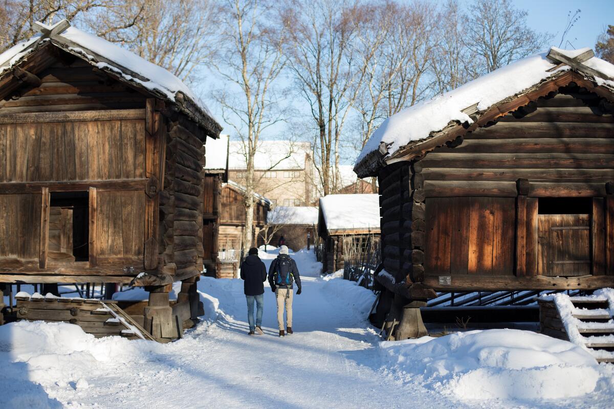 To menn går tur i Friluftsmuseet forbi to stabbur