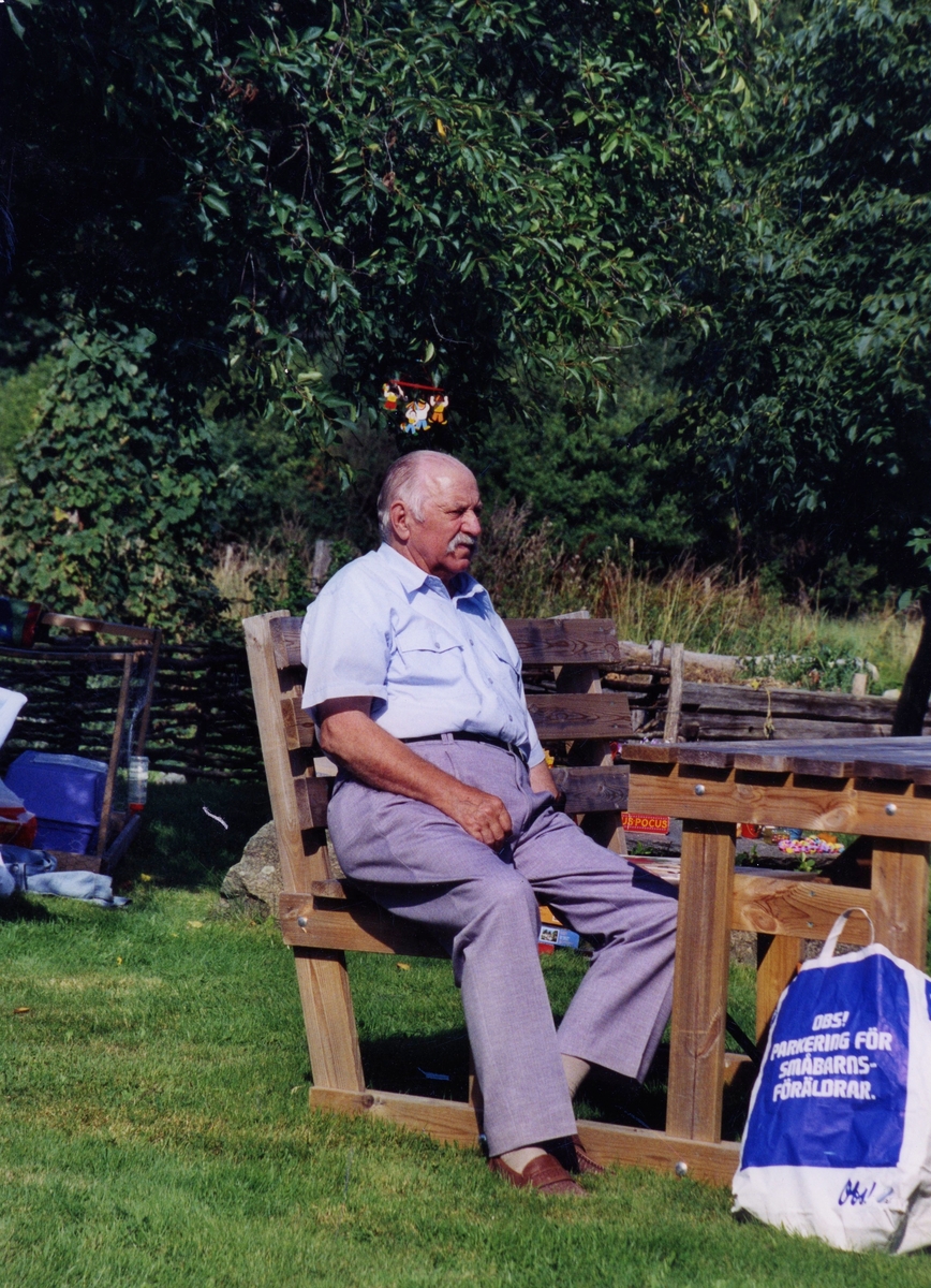Olle Bengtsson (1918 - 2006) sitter i en trädgårdsmöbel utanför Hembygdsgården Långåker 1:3 cirka år 2000.