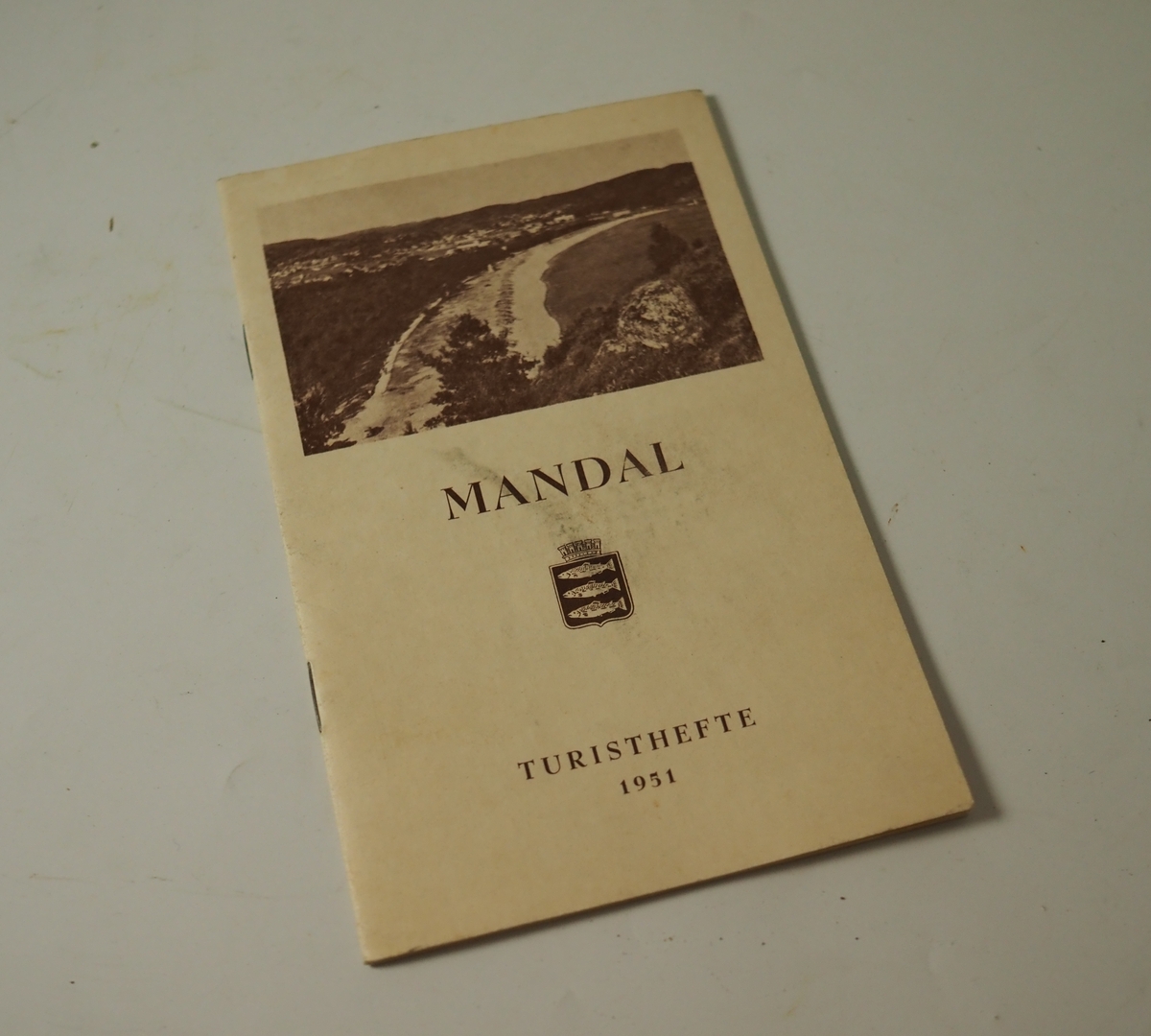 Turisthefte for Mandal by fra 1951. Innholder informasjon om Mandal, kart over byen og annonser for noen av byens bedrifter.