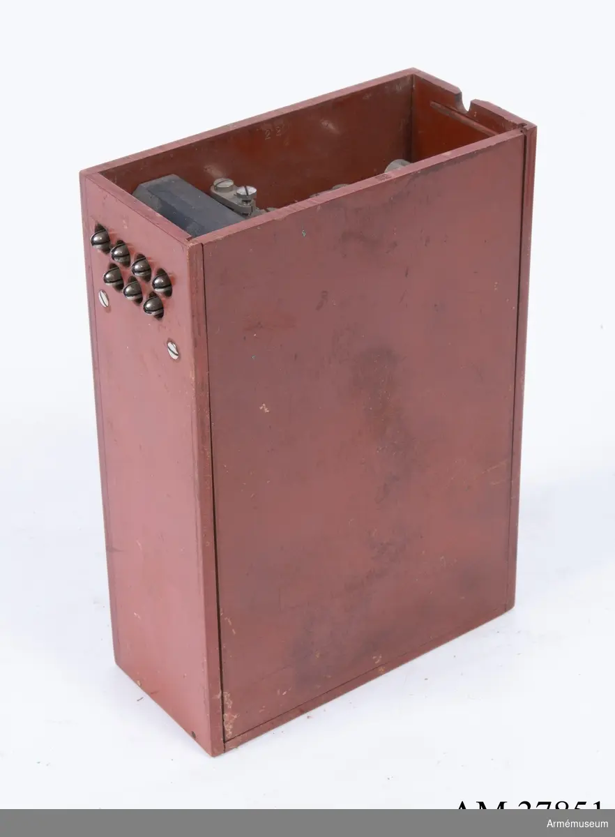 Grupp H I.
Fälttelefonapparat m/1909 med 7-delig propp.
Fiberlåda med innehåll. Utan hörnbeslag. Saknas: lådans lock med tillhöriga delar, batteri, induktionsrulle.