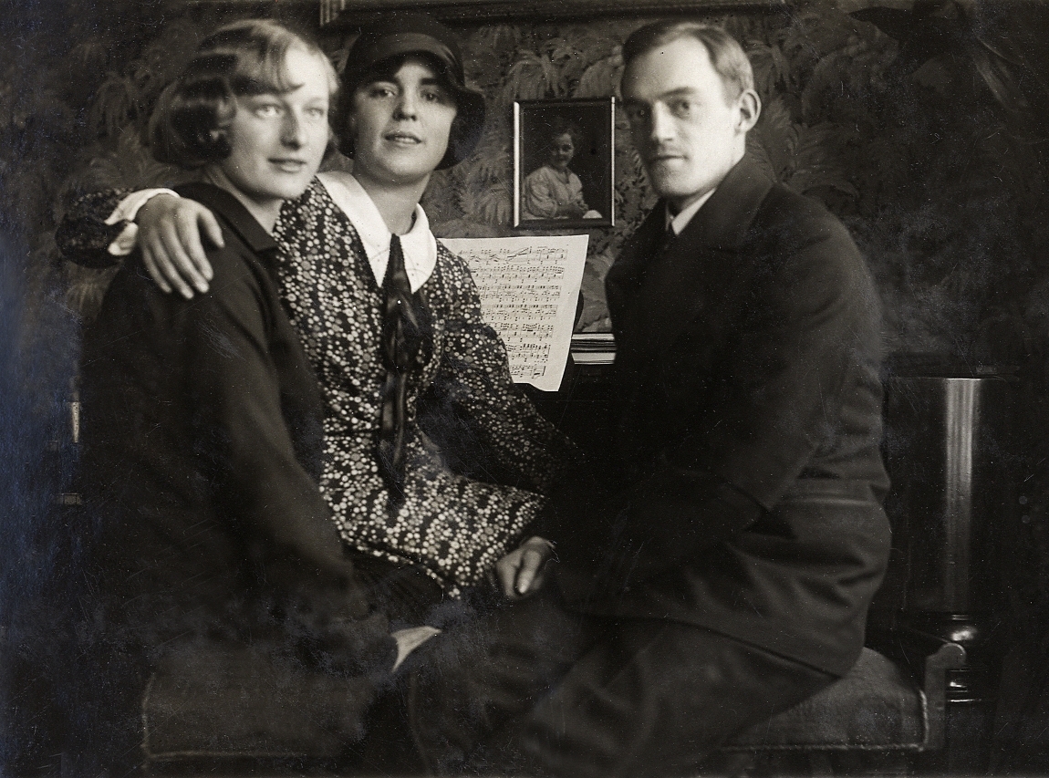 Två kvinnor och en man sitter på en pianopall invid ett piano.
Under fotot text: "Brita, Ruth o Gösta".
