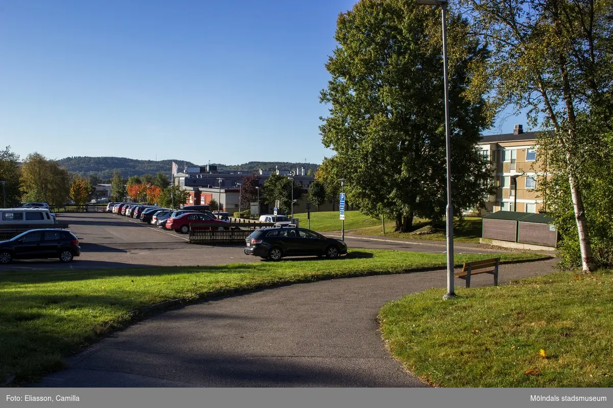 Vy från Valåsvägen mot bebyggelse i Lindome den 4 oktober 2016. Till vänster ses en parkeringsplats, i mitten affärsbebyggelse i Lindome centrum samt till höger bostadsbebyggelse i Smörkullegården. Vy mot sydväst.
