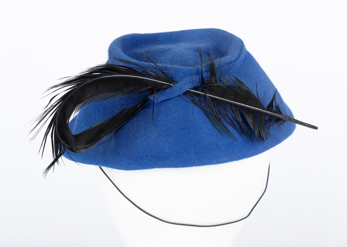 Filthatt med fjær, tilnærmet bøtteformet hattepull.
Lang svart fjær.
Fabrikk \ typemerke: La Familiare