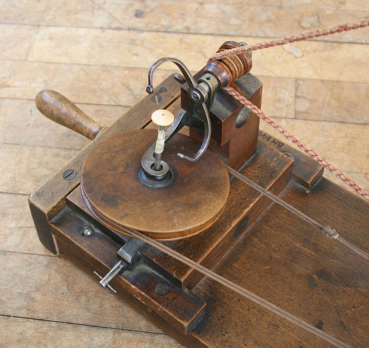 Maskinen är byggd på en träplatta. På plattan ett handvevat hjul som genom ett snöre driver en bygel som lindar garnet runt knappen. Knappen roterar runt. Märkt: M. GRIEBEL MAGDEBURG

Funktion: Lindning av trådknappar