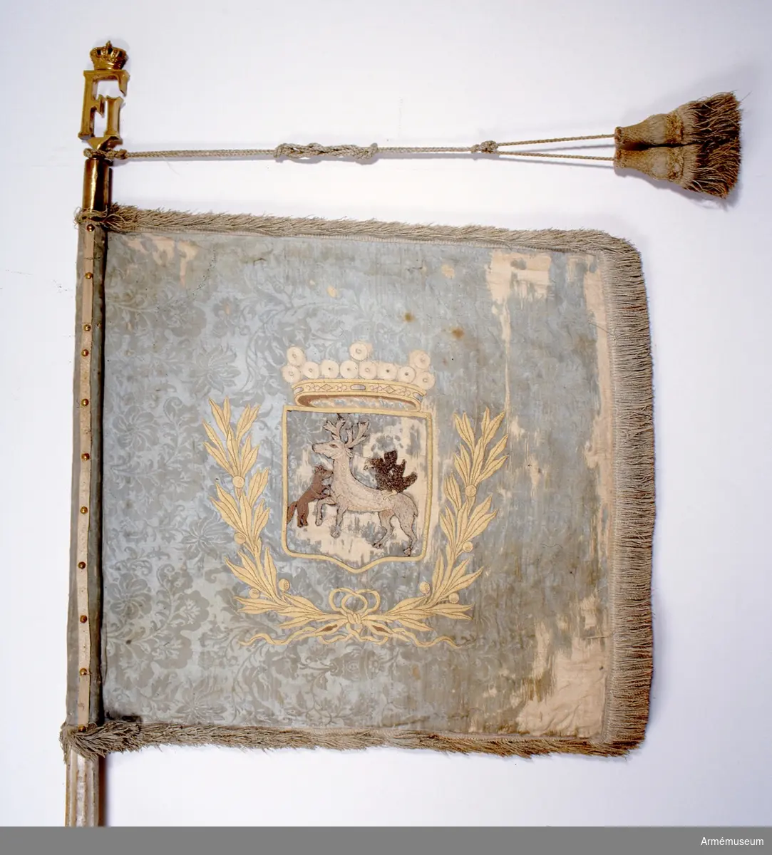 På ljusblå duk Jämtlands landskapsvapen under öppen krona samt omgiven av en lagerkrans. Motivet broderat. Duken är konserverad. Originalkordongerna är bevarade men spetsen på standaret är inte original.