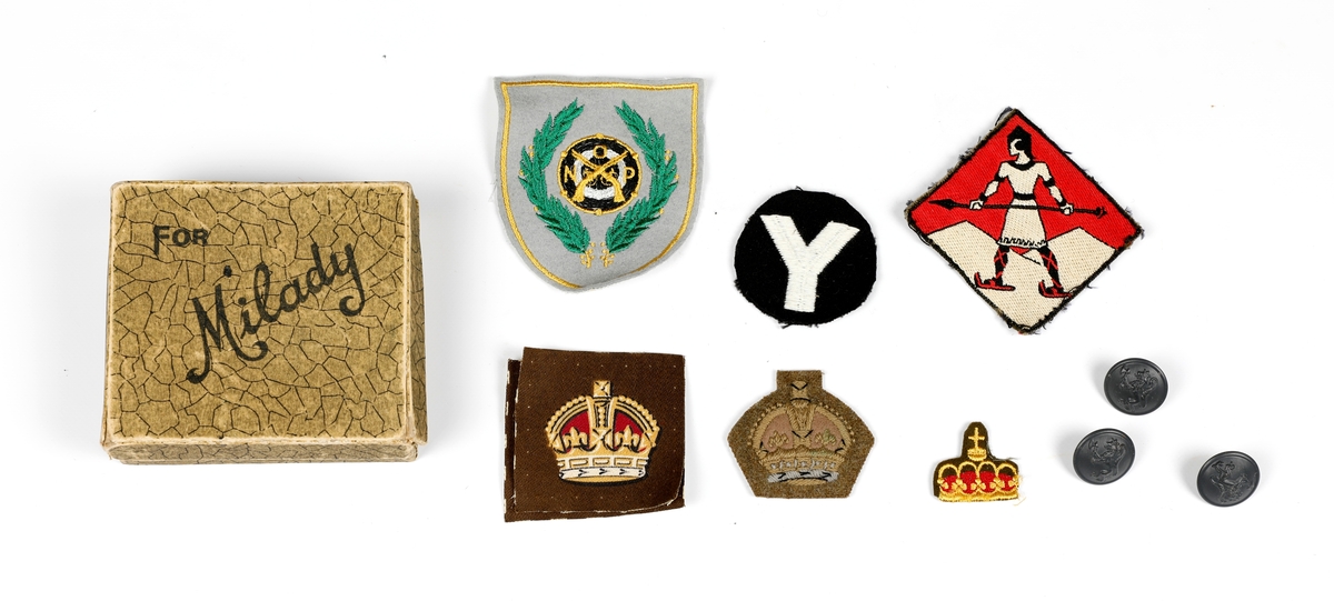 Eske med forskjellige britiske militærmerker fra tysklandsbrigaden (5 stk), hvor et merke er fra Yorkshirebrigaden, et merke fra østoppland regiment (1955-1983), norske offiseres pistolklubb (?) (1 stk.) og norske militærknapper (3 stk.).