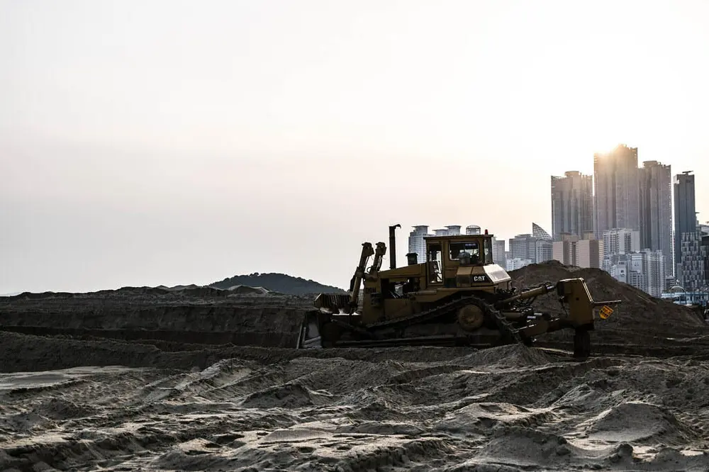 Foto av en bulldoser på et anleggsområde med en bysilhuett i bakgrunnen