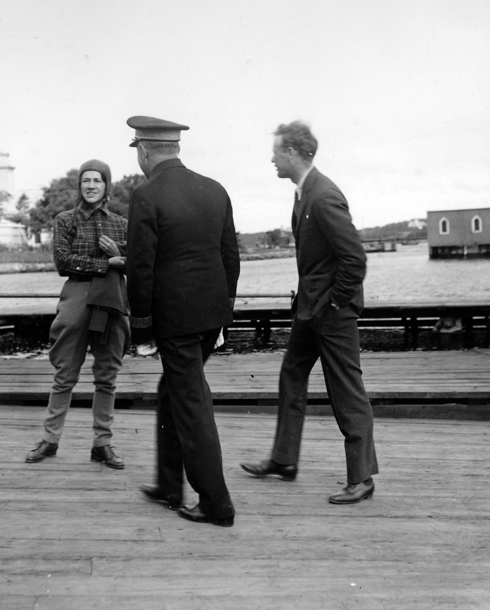 Anne Morrow Lindbergh och Charles Lindbergh står på en brygga vid besök på F 2 Karlskrona flygstation på Stumholmen i september 1933. I mitten står en svensk militär.
