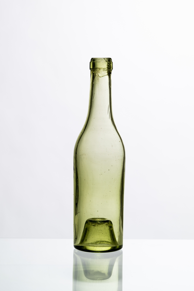 Brännvinsflaska av ljust grönt glas (mindre storlek), avsedd för tillslutning med naturkork. Flaskan har "Kinnekullebotten" med liten kula. Blåsor i glaset. Hantverksmässigt tillverkad vid Sunds glasbruk, Jönköpings län. Se vidare Historik.