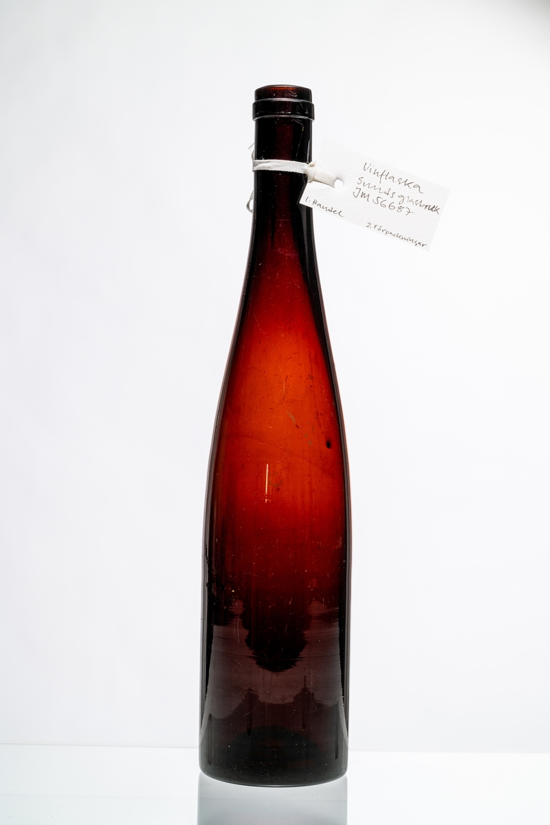 Vinflaska, fransk modell, av röd-brunt glas, avsedd för tillslutning med naturkork. Flaskan tillverkades även i grön färg. Hantverksmässigt tillverkad vid Sunds glasbruk, Jönköpings län. Se vidare Historik.
