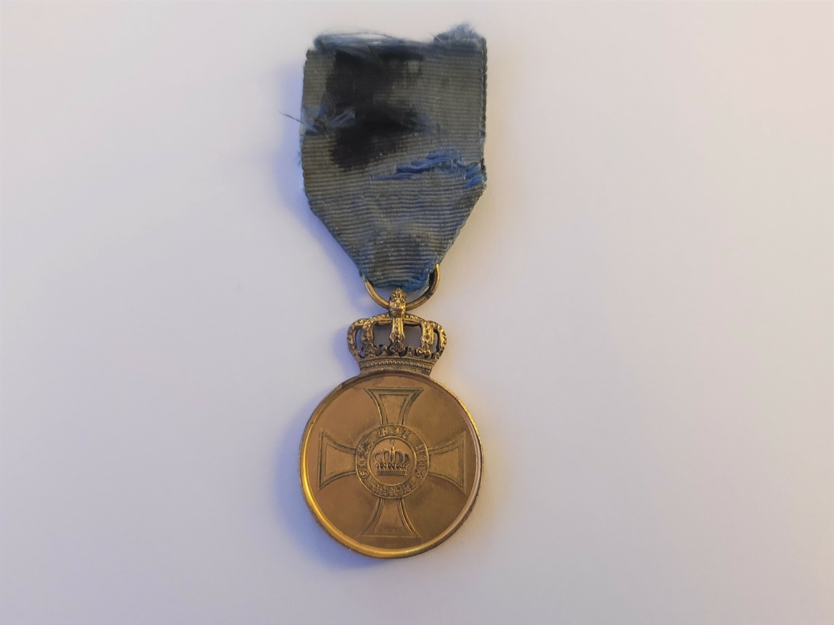 Keiserlosmedaljen bærer en krone innlemmet inne i et kors på advers. Medaljen er opphengt i et blått bånd som har noen skader.