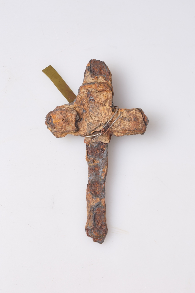 Forrustet kors eller beslag av jern, mest sannsynlig rester av et beslag. Heimesmidd, klumpete, funnet i hagen.