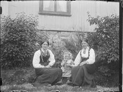 To kvinner og et jentebarn oppstilt i pentøy utenfor Klokker