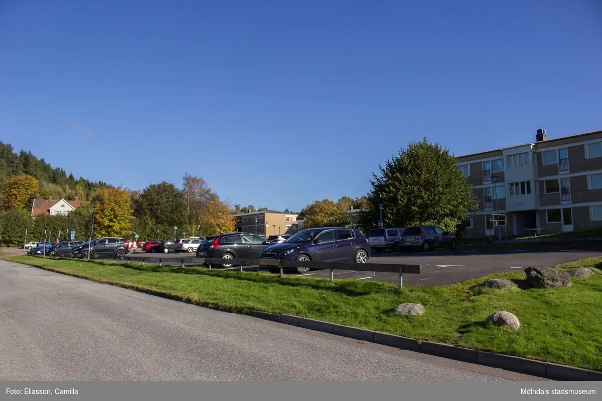 Vy  från Sagbrovägen, över en parkeringsplats, mot bebyggelse i bostadsområdet Dotegården. Lindome den 4 oktober 2016. Till vänster ses även övre delen av bostadshuset Sagbrovägen 36. Vy mot nordost.