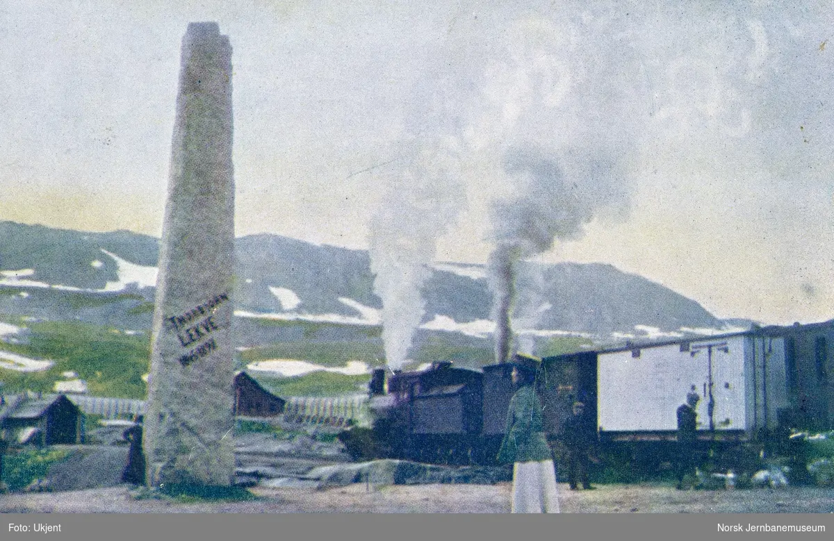 Damplokomotiv type 21a med tog retning Bergen på Finse stasjon. I forgrunnen bauta til minne om NSB overingeniør Thorbjørn Lekve (1845-1897)