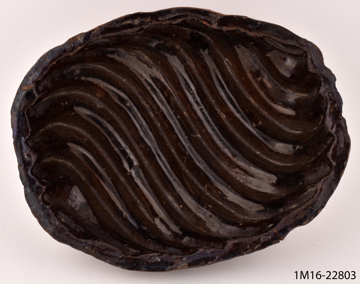 Puddingform av lergods med mörkbrun glasyr, med snäckformig utformning.