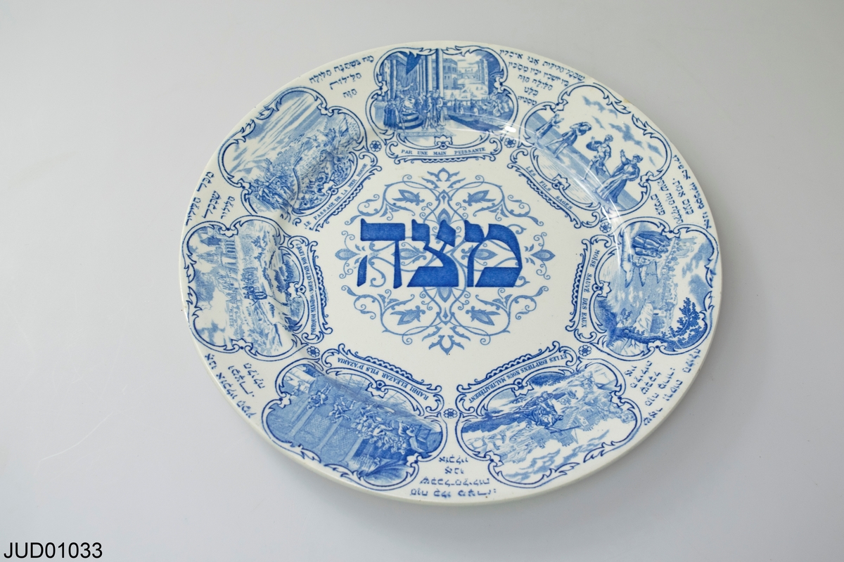 Rund tallrik i porslin med blått tryck. Text "matsa" på hebreiska och scener ur Amsterdamhaggadan.